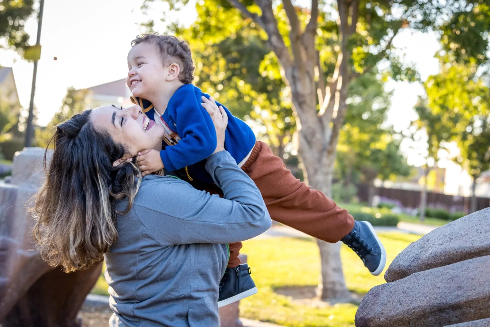 A mother lifting her laughing toddler in a park at golden hour