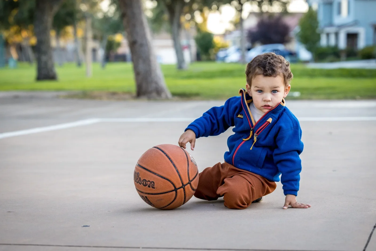 A toddler kneeling with a basketball on an outdoor court